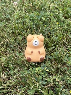 A small capybara squishy placed on green grass outdoors.